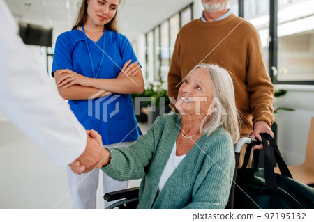 Senior woman on wheelchair meeting doctor in hospital, shaking hands. 97195132