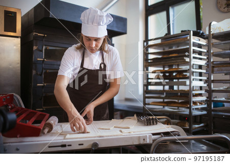 Young baker with chef cap preparing pastries in bakery. Young baker with chef cap preparing pastries in bakery. 97195187