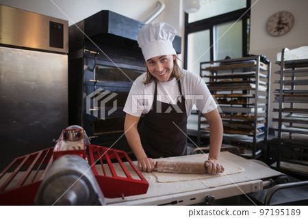 Young baker with chef cap preparing pastries in bakery. 97195189