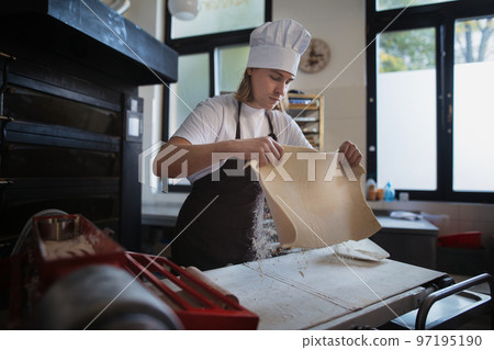 Young baker with chef cap preparing pastries in bakery. Young baker with chef cap preparing pastries in bakery. 97195190
