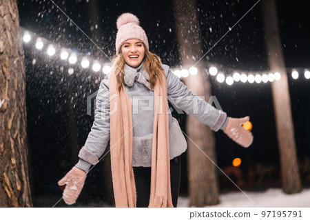 A beautiful girl is playing with snow. Happy winter time in the forest. Festive garland lights. Christmas. 97195791