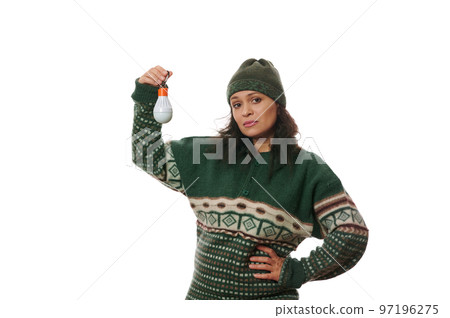 Young pretty woman wearing warm wool green sweater, feels stressed, anxious or scared, holds a flashlight bulb, suffering from the electricity interruption, isolated on white background. Copy space Young pretty woman wearing warm wool green sweater, feels stressed, anxious or scared, holds a flashlight bulb, suffering from the electricity interruption, isolated on white background. Copy space 97196275