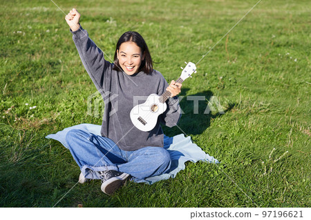 Excited asian girl sits in park with ukulele, plays instrument and feels happy upbeat, positive moments and people concept Excited asian girl sits in park with ukulele, plays instrument and feels happy upbeat, positive moments and people concept 97196621