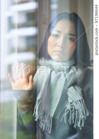 Asian woman feels unwell, stays at home, looks outside window with jealous, distressed face, wants go outside but caught cold 97196644