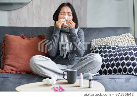 Young asian woman staying at home, feeling unwell, catching a cold, sick leave, sneezing, drinking hot tea and taking medication Young asian woman staying at home, feeling unwell, catching a cold, sick leave, sneezing, drinking hot tea and taking medication 97196648