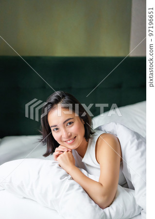 Vertical shot of smiling korean woman lying on pillow in her bed, spending morning in bedroom, waking up from sleep, looking happy Vertical shot of smiling korean woman lying on pillow in her bed, spending morning in bedroom, waking up from sleep, looking happy 97196651