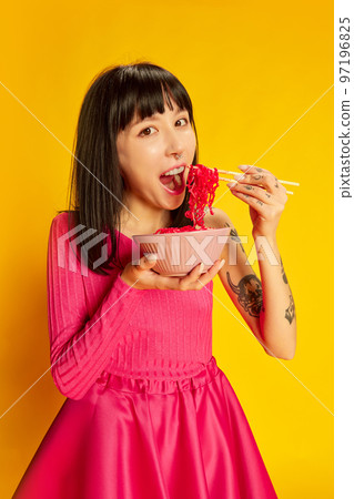 One young beautiful girl in bright pink dress posing with pink noodles isolated on vivid yellow background. Concept of youth, beauty, fashion, lifestyle, emotions 97196825