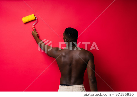 African painter focused on work holding professional roller to paint an interior wall, studio. African painter focused on work holding professional roller to paint an interior wall, studio. 97196930