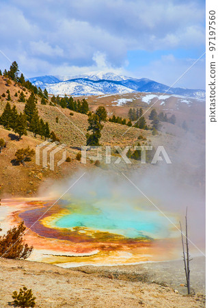 View of steamy hot spring from above overlooking snowy mountains by Yellowstone View of steamy hot spring from above overlooking snowy mountains by Yellowstone 97197560