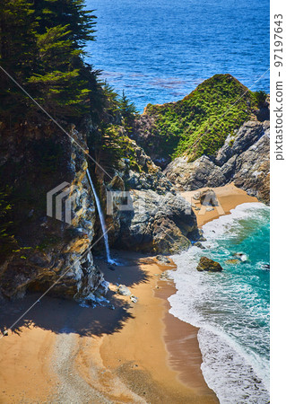 View of hidden waterfall from cliffs into sandy beaches by ocean waves 97197643