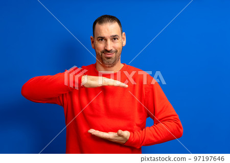A man holding an object with both hands in front of him, displaying, offering or advertising an object against a blue wall. Empty. Space. Concept. Object. Background. Portrait. Copy A man holding an object with both hands in front of him, displaying, offering or advertising an object against a blue wall. Empty. Space. Concept. Object. Background. Portrait. Copy 97197646