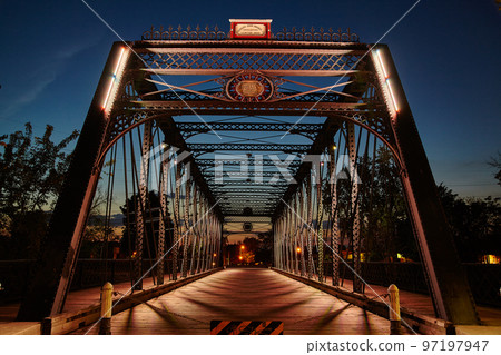 Metal bridge leading into downtown lit by street lamplight at dusk Metal bridge leading into downtown lit by street lamplight at dusk 97197947