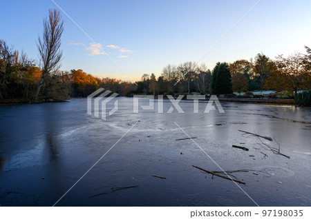 A frozen lake at sunset. There is ice on the surface of the lake in this winter scene. A cold winter's day in Kelsey Park, Beckenham, Kent, UK. A frozen lake at sunset. There is ice on the surface of the lake in this winter scene. A cold winter's day in Kelsey Park, Beckenham, Kent, UK. 97198035