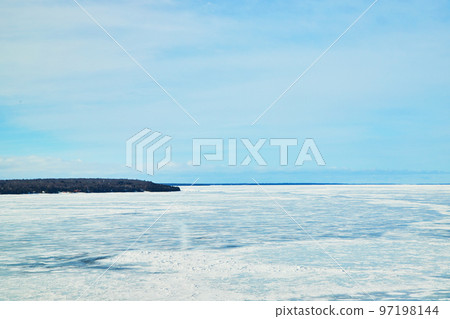 View of land from frozen lake covered in ice View of land from frozen lake covered in ice 97198144