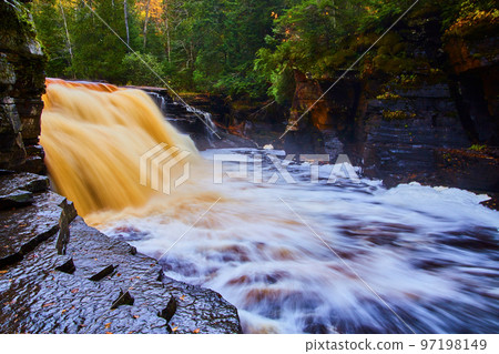 Wet rock path with giant golden and brown waterfall in a deep green forest 97198149