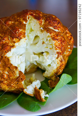 Cross section of a seasoned and cooked head of cauliflower on a bed of greens Cross section of a seasoned and cooked head of cauliflower on a bed of greens 97198242