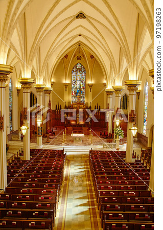 White interior of a cathedral from the balcony showing the pews and altar and stained glass altar in the sanctuary 97198263