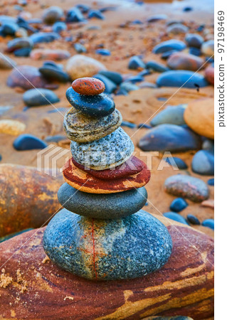 Stone cairn with multicolored stones and an orange beach Stone cairn with multicolored stones and an orange beach 97198469