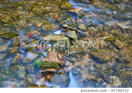 Small moss-covered rocks in a shallow riverbed Small moss-covered rocks in a shallow riverbed 97198532