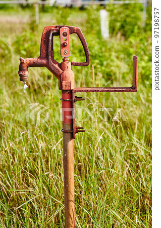 Rusted orange water spigot in wild tall grasses Rusted orange water spigot in wild tall grasses 97198757
