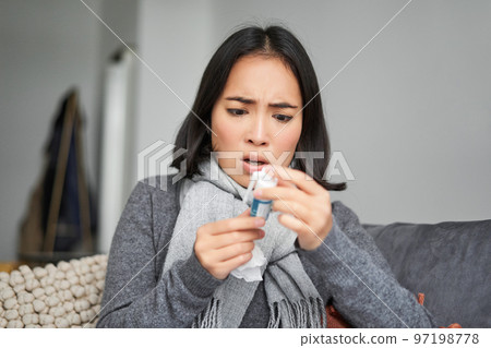Ill korean woman looking at thermometer with concerned face, catching cold, having fever, having covid, staying at home on sick leave Ill korean woman looking at thermometer with concerned face, catching cold, having fever, having covid, staying at home on sick leave 97198778