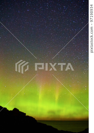Starry night with wave of green aurora lights out over a large lake ocean or sea with coast silhouette Starry night with wave of green aurora lights out over a large lake ocean or sea with coast silhouette 97198934