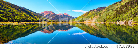 Panorama of lake in the mountains surrounded by fall trees and red sandy mountain peaks 97198953