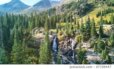 Waterfall tucked into valley of mountains surrounded by pine trees Waterfall tucked into valley of mountains surrounded by pine trees 97199447