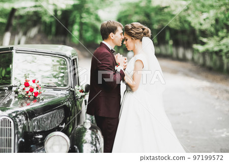 Beautiful newlywed couple posing near retro black car Beautiful newlywed couple posing near retro black car 97199572