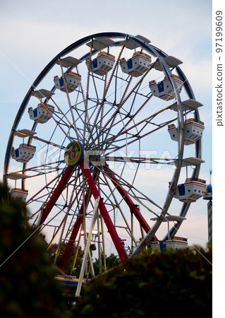 Large red ferris wheel backlit against a hazy light blue sky 97199609