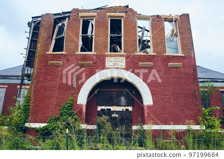 Small abandoned high school of red brick with broken windows and no trespassing signs 97199684