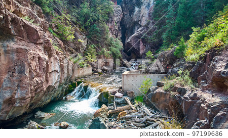 Large canyon with cement wall and waterfall over rocks 97199686