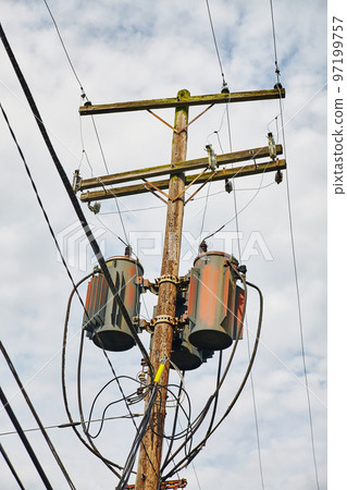 Old wooden telephone pole with grain elevators against a cloudy sky Old wooden telephone pole with grain elevators against a cloudy sky 97199757