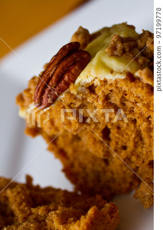 Orange muffins with frosting and a pecan topping on a white plate against an orange background 97199778