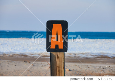 Signpost marker letter A on sandy beach with icy layer 97199779