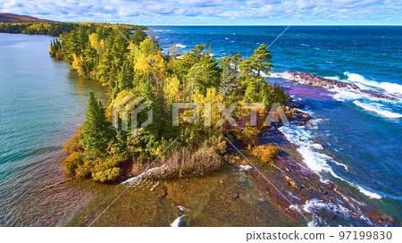 Ocean lake or sea with an island of trees and a red beach and a brown beech and a forest with fall colors of green, orange, yellow and red 97199830