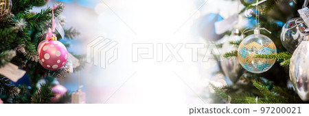 Web banner of winter holidays. Close up of colorful decorative balls on christmas trees branches. Defocused lighting garlands in background. Copy space. Concept of New Year celebration 97200021