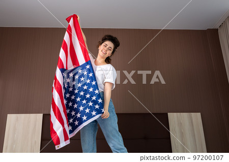 A young happy woman dances with an American flag. Bottom view. Indoor. The concept of the American national holidays and patriotism A young happy woman dances with an American flag. Bottom view. Indoor. The concept of the American national holidays and patriotism 97200107