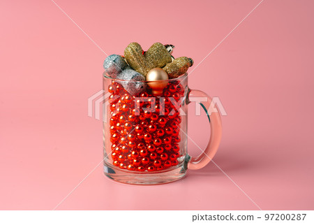 Glass with Christmas decorations on pink pastel background Glass with Christmas decorations on pink pastel background 97200287