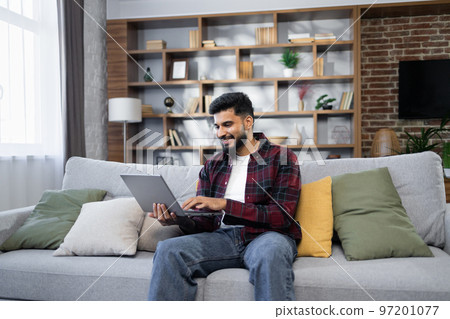 Bearded young man using laptop, sitting on couch at home, handsome guy having video call Bearded young man using laptop, sitting on couch at home, handsome guy having video call 97201077