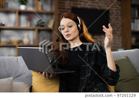 Closeup of young student woman in wireless headset watching online lesson on laptop Closeup of young student woman in wireless headset watching online lesson on laptop 97201129