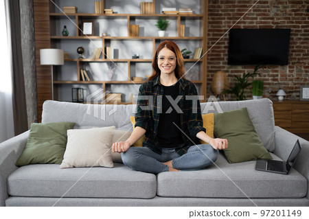 Calm of caucasian young woman doing yoga lotus pose to meditation and relax on couch during work 97201149