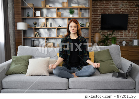 Calm of caucasian young woman doing yoga lotus pose to meditation and relax on couch during work 97201150
