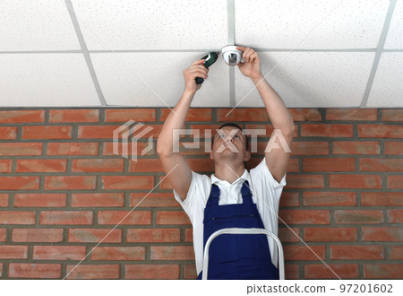 Technician installing CCTV camera on ceiling indoors Technician installing CCTV camera on ceiling indoors 97201602