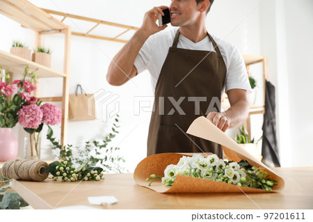 Florist with beautiful flowers talking on smartphone in workshop, closeup Florist with beautiful flowers talking on smartphone in workshop, closeup 97201611