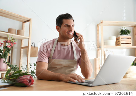 Florist talking on smartphone near laptop in workshop Florist talking on smartphone near laptop in workshop 97201614