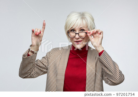 beautiful elderly woman with glasses shows her index finger up. advertising concept of a business woman leader beautiful elderly woman with glasses shows her index finger up. advertising concept of a business woman leader 97201754