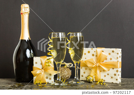 Champagne bottle with confetti, glasses and christmas decor on colored holiday background. Flat lay New Year decorations Champagne bottle with confetti, glasses and christmas decor on colored holiday background. Flat lay New Year decorations 97202117