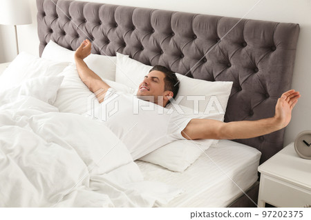 Man awakening on bed at home. Lazy morning 97202375