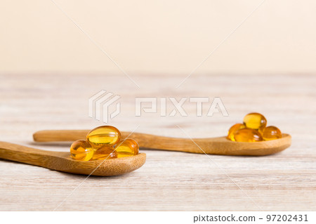Vitamin omega capsules in a spoon on a colored background. Pills served as a healthy meal. Red soft gel vitamin supplement capsules on spoon 97202431